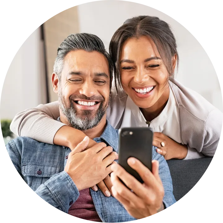A man and woman are smiling while looking at a cell phone.
