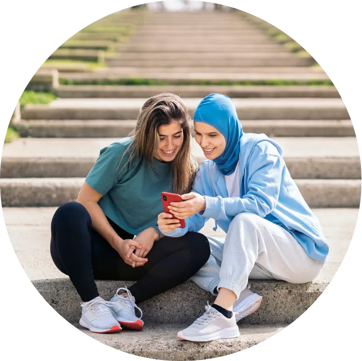 Two women sitting on steps looking at a cell phone.