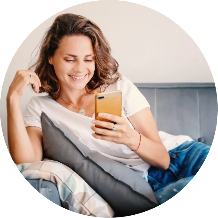A woman sitting on a bed looking at her cell phone.